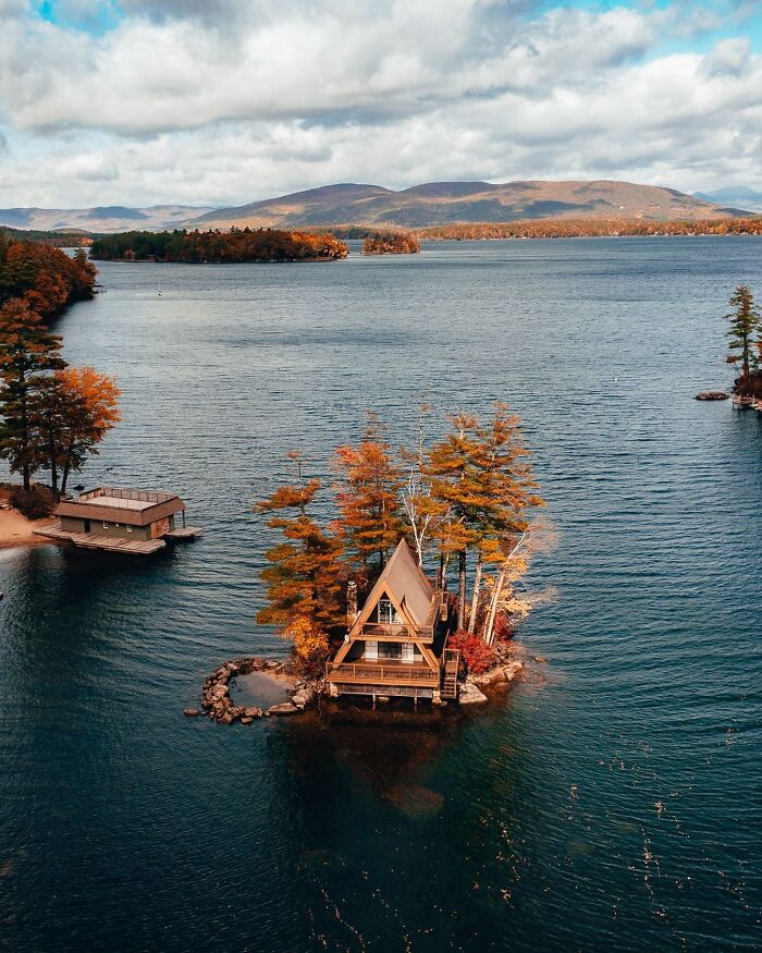 Beautiful architecture: A small, charming cabin on a tiny island surrounded by vibrant autumn trees and a vast lake.
