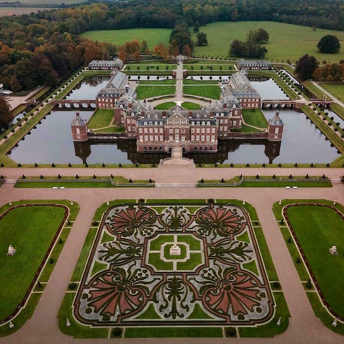Aerial view of beautiful architecture, a grand castle surrounded by a moat and elaborate formal gardens.