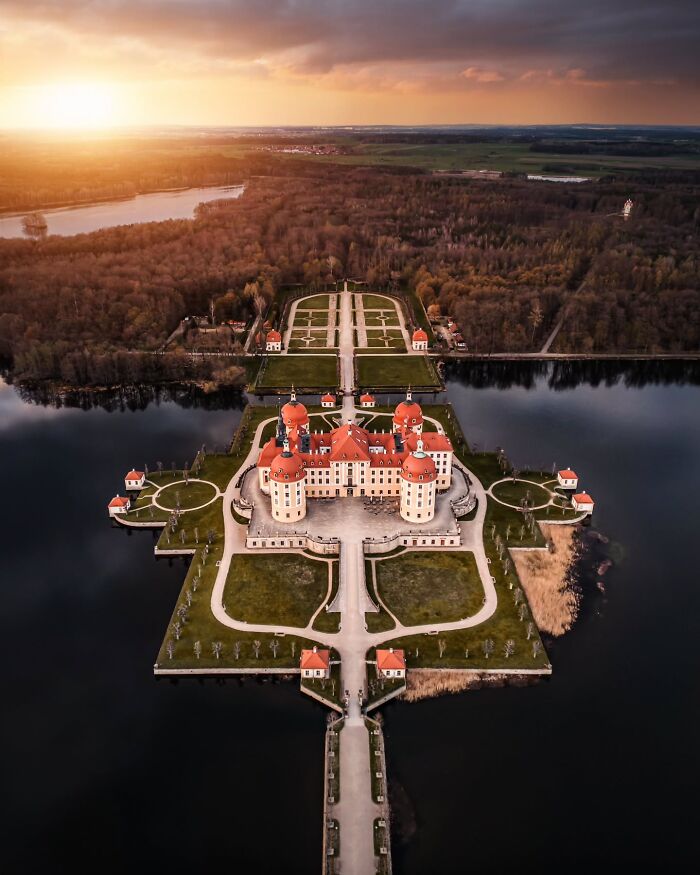 Beautiful architecture of a fairytale castle surrounded by water and extensive gardens at sunset.