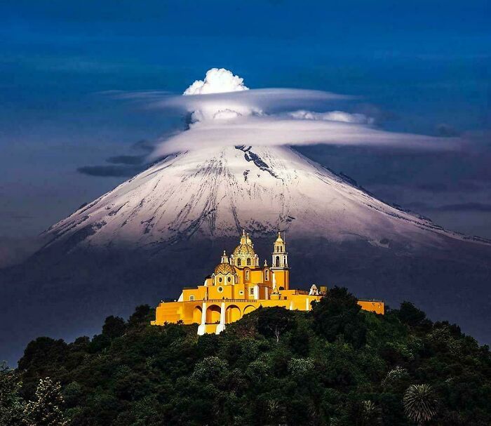 Beautiful architecture of a vibrant yellow church nestled on a hill with a majestic, snow-capped mountain in the background.