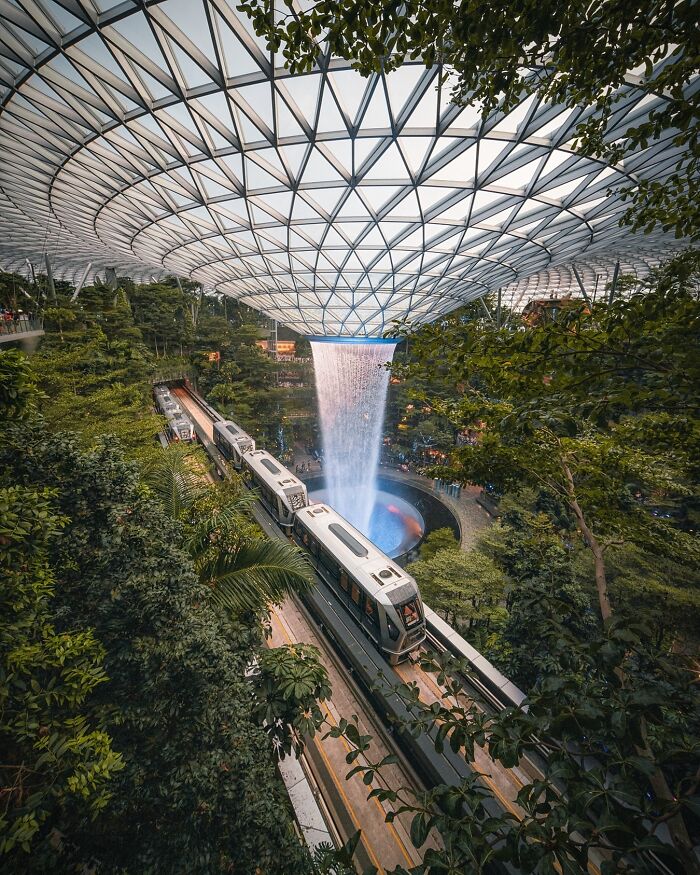 Stunning architecture with a modern train passing by a beautiful indoor waterfall surrounded by lush greenery.