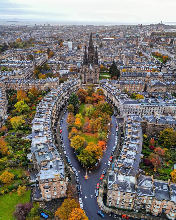 Aerial view of a European city street curving around an autumn-colored park, showcasing beautiful architecture and urban planning.