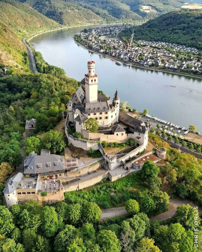 Aerial view of a historic castle nestled by a winding river and lush green hills, an example of beautiful architecture.