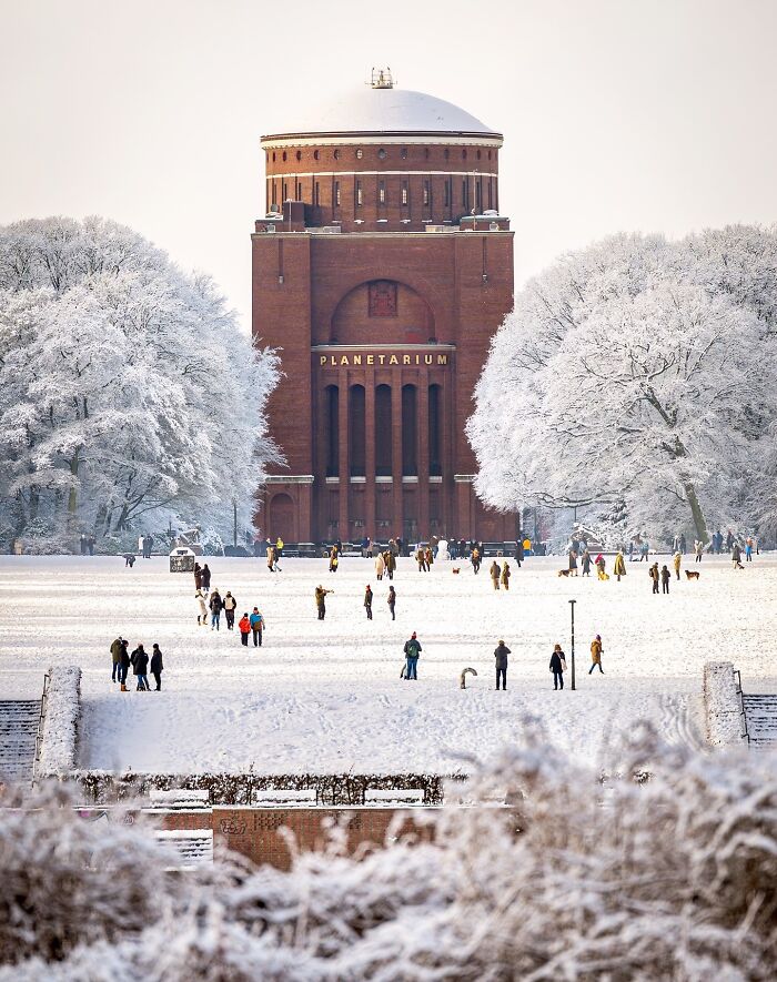 A majestic, beautiful brick planetarium building in a snowy landscape, surrounded by white trees and people.