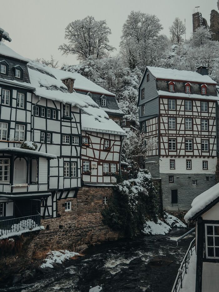 Snow-covered, beautiful architecture of half-timbered houses along a river, nestled in a winter wonderland.