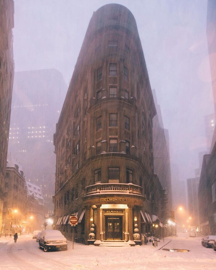 A beautiful, snow-covered triangular architecture of a building, Delmonico's, lit up at night, creating an unreal scene.