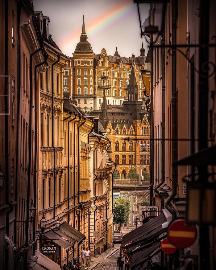 Narrow European street with beautiful architecture, featuring historic buildings and a rainbow in the sky.