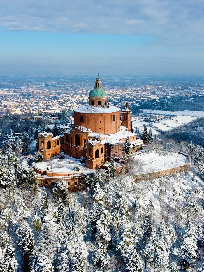 Magnificent architecture of a large basilica on a hilltop, surrounded by snow-covered trees and a city in the distance.