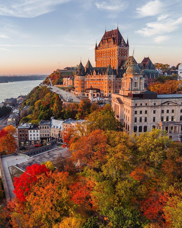 Breathtaking architecture of a grand hotel and surrounding buildings overlooking a river, with vibrant autumn trees.