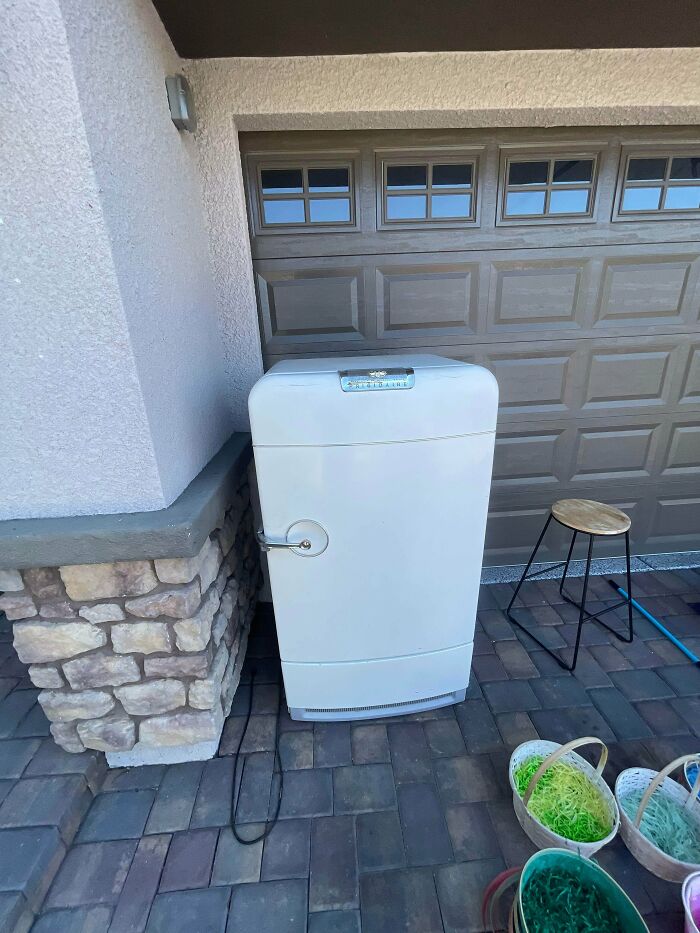 Vintage white refrigerator thrift store find placed outside near stone wall and garage door on tiled patio.