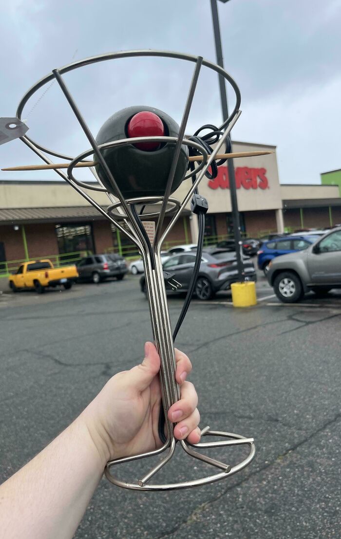 Hand holding a unique vintage thrift store find resembling a martini glass with a black and red ball inside.