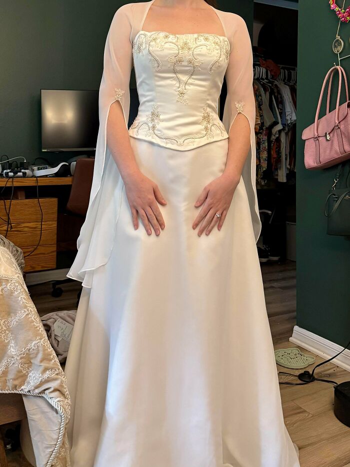 Woman wearing an elegant white wedding dress found as a thrift store find, featuring embroidered bodice and sheer sleeves.