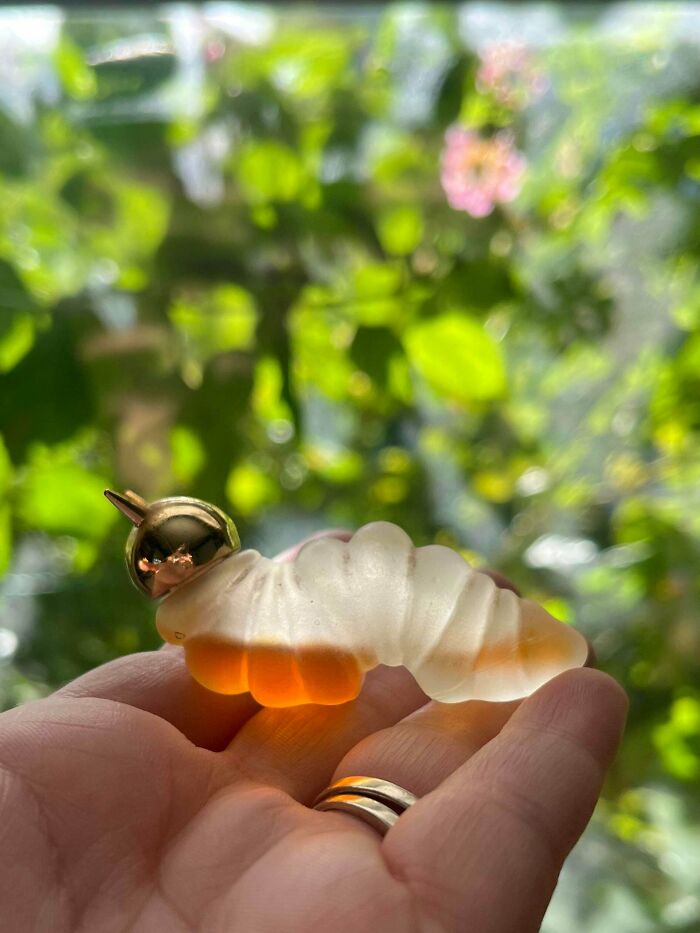 Hand holding a translucent caterpillar figurine with a gold helmet, a unique thrift store find glowing in natural light.