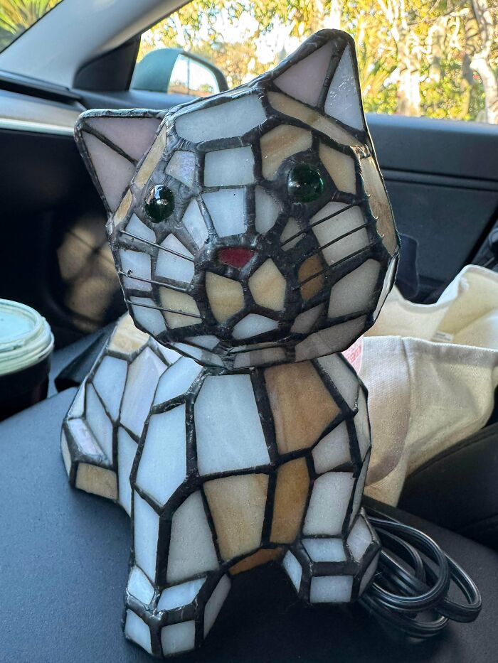 Stained glass cat lamp thrift store find with beige and white panels sitting on car seat surrounded by bags and cords.