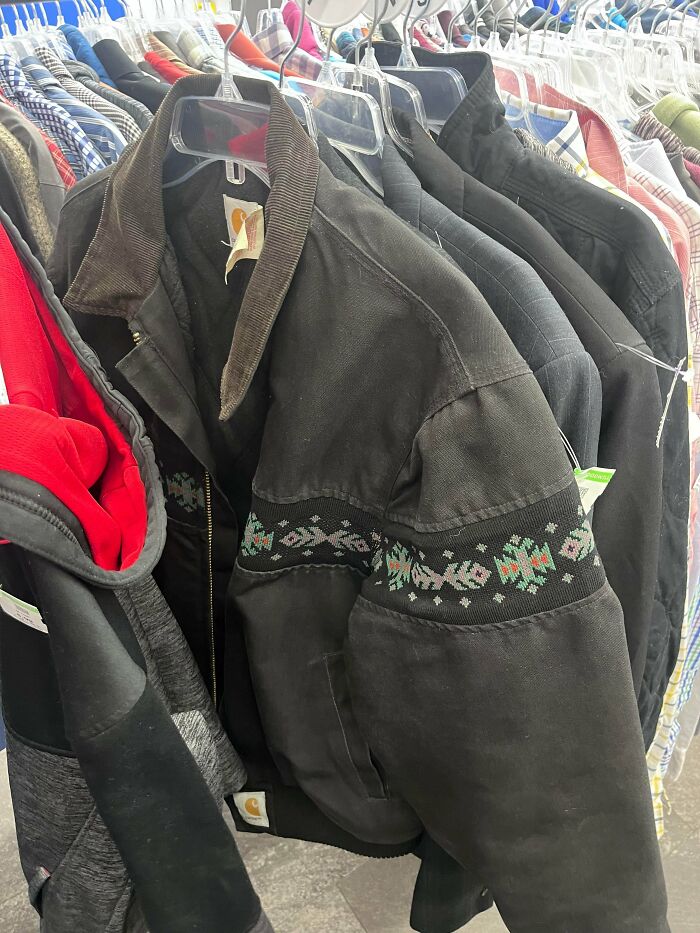 Black patterned jacket among thrift store finds hanging on rack with various other clothes and jackets.
