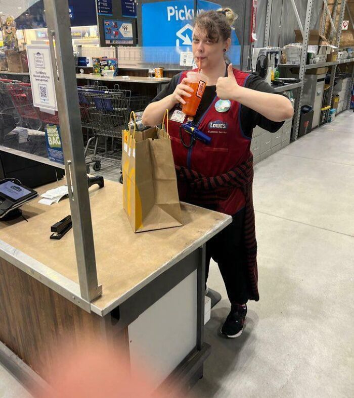 Delivery confirmation pic of a store employee giving thumbs up while holding a drink next to a paper bag on the counter.