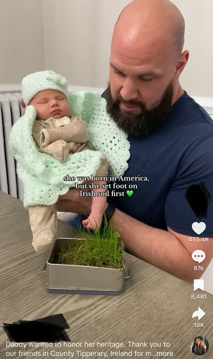A man holding an American baby with her foot touching a small box of grass to set foot on Irish soil first