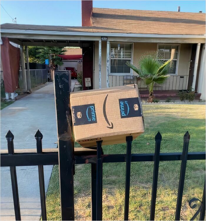 Amazon Prime delivery box stuck on metal fence post as a hilarious delivery confirmation pic sent by driver to customer outside a home.