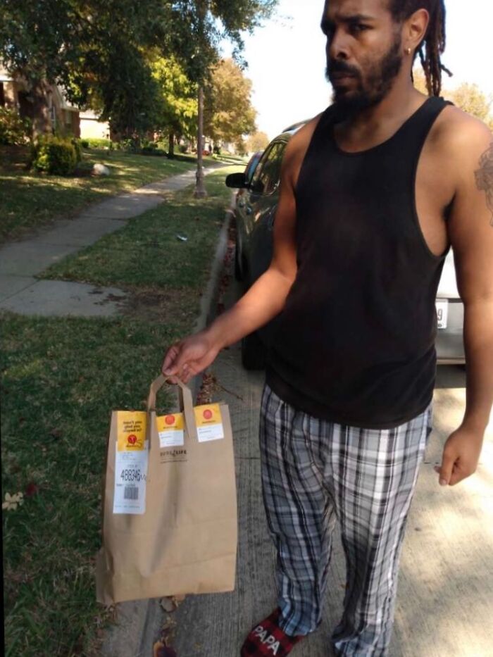 Delivery driver in casual clothes holding a paper bag on a suburban sidewalk for delivery confirmation pics.