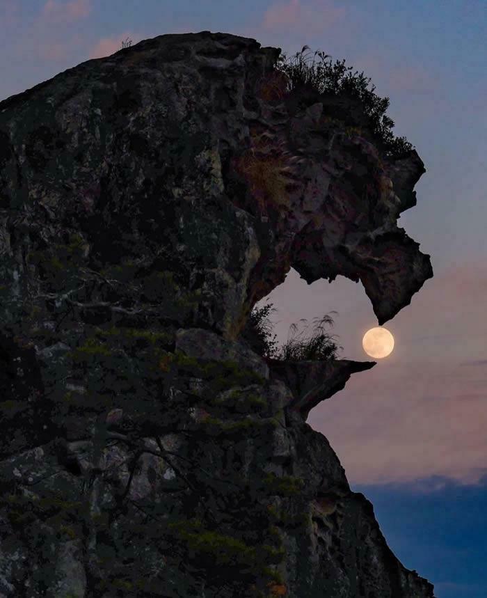 An amazing photo of a full moon perfectly framed by a rock formation, resembling a creature holding the moon.