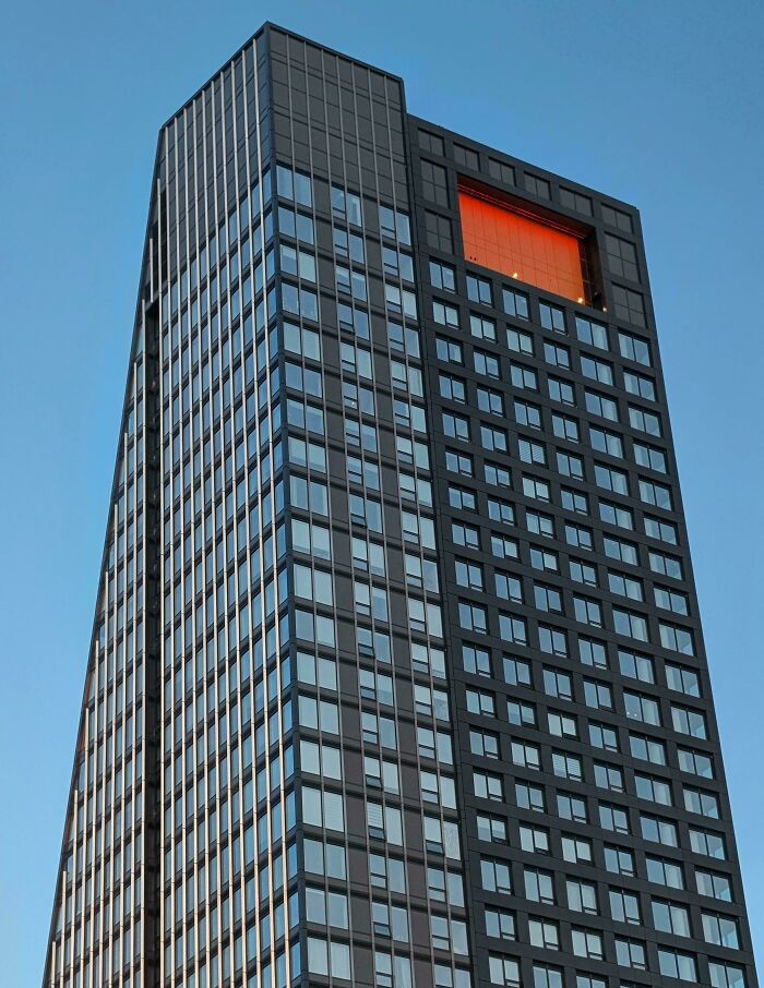 A dark skyscraper with one prominent orange window, resembling a building for an evil mastermind.