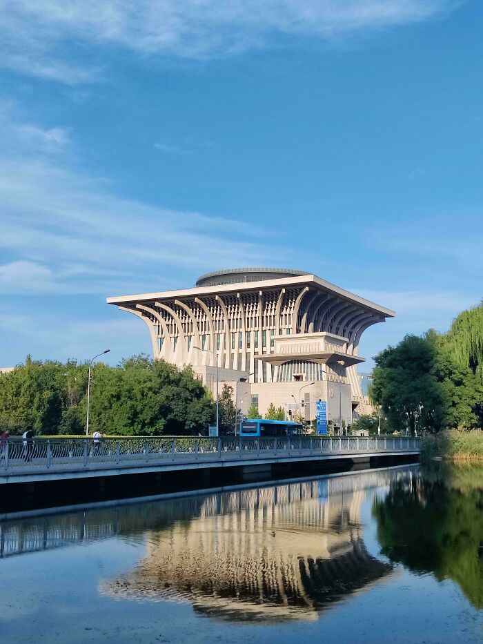 An elaborate, modern building, ideal for an evil mastermind, reflected in a tranquil body of water under a blue sky.