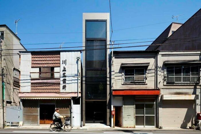 A narrow, modern building with a glass facade, a perfect evil mastermind building, nestled between traditional Japanese shops.