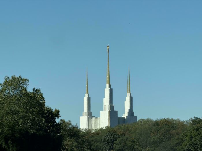 A tall, white building with three spires, seemingly built for an evil mastermind, peeking above trees.