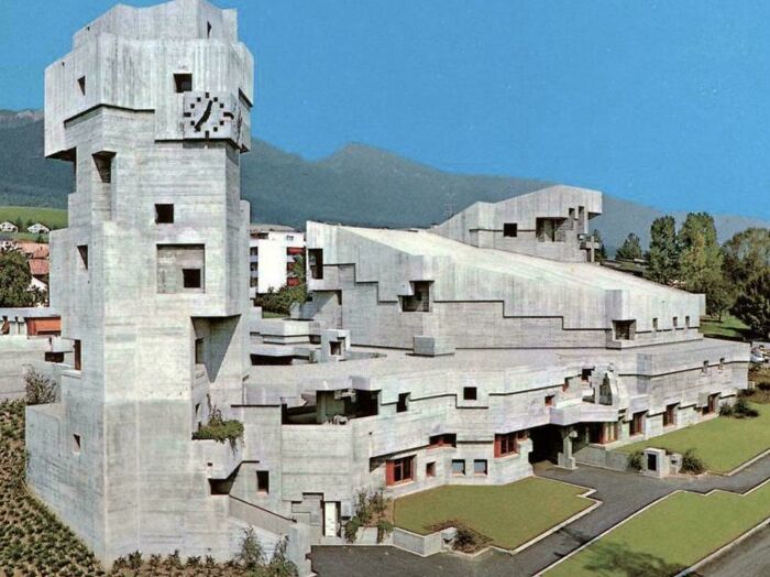 An unusual, blocky concrete building, resembling one built for an evil mastermind, against a mountain backdrop.