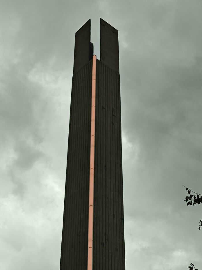 A tall, slender concrete structure with a pink vertical stripe against a cloudy sky, suitable for an evil mastermind.