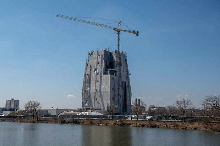 An unusually shaped building under construction by a lake, resembling a lair for an evil mastermind.