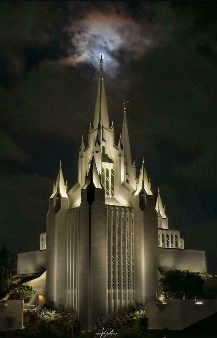 An illuminated, spired building, possibly for an evil mastermind, under a full moon at night.
