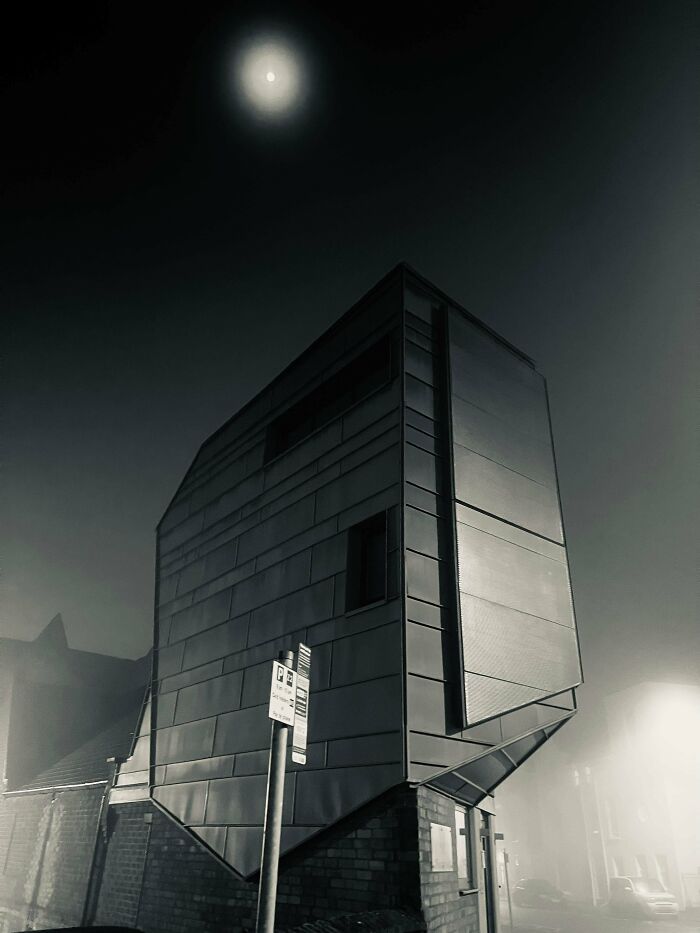 A modern, dark building with a unique, angular design under a full moon, perfect for an evil mastermind.