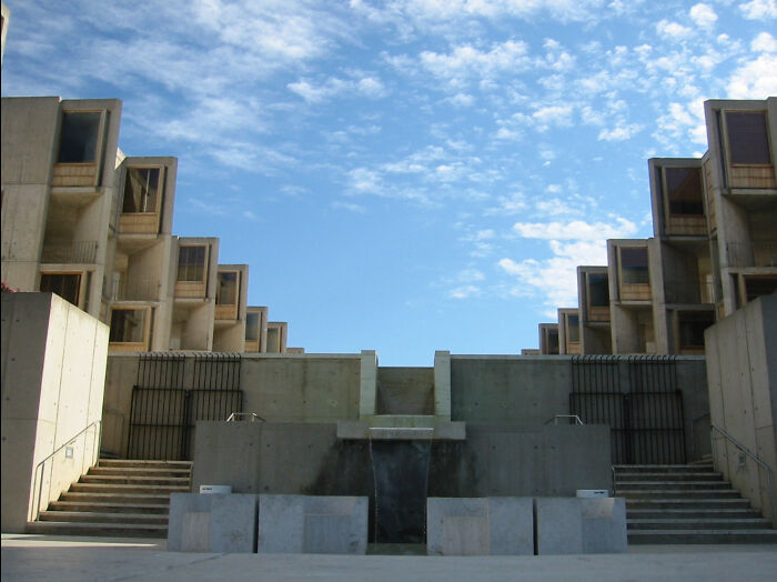 Symmetrical concrete buildings with a central fountain under a blue sky, designed for an evil mastermind.