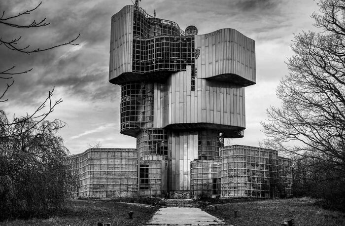 A dilapidated, brutalist evil mastermind building with a complex, grid-like facade in a desolate, black and white landscape.