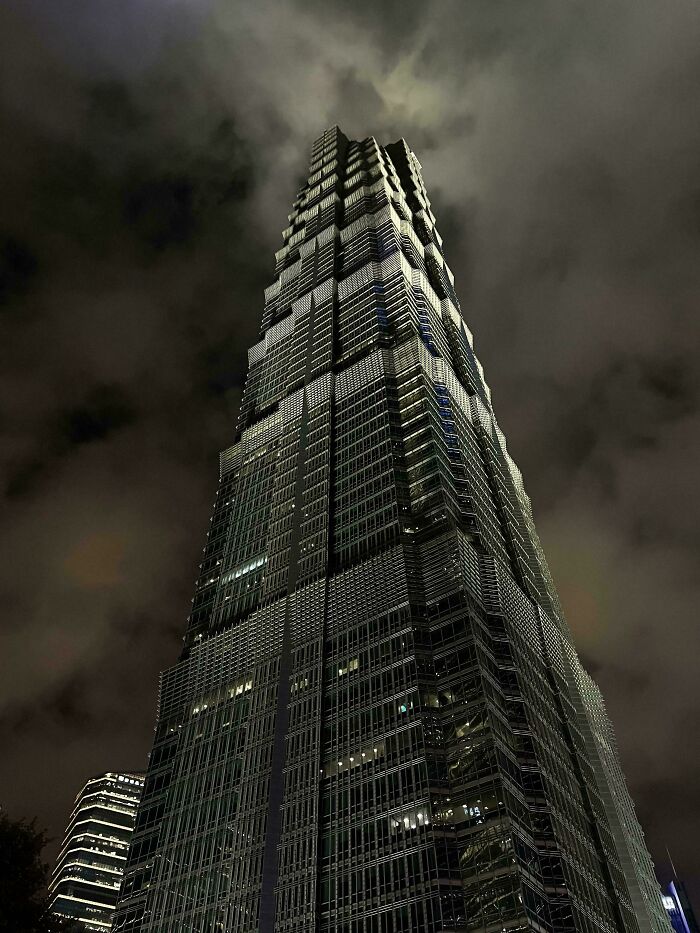 A towering, modern evil mastermind building piercing a dramatic, cloudy night sky, an ideal base for world conquest.
