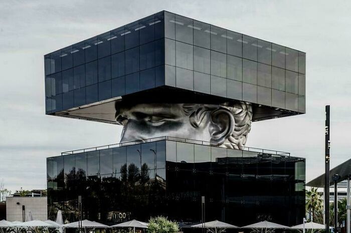 A striking building with a giant head sculpture between two mirrored glass blocks, an evil mastermind's headquarters.