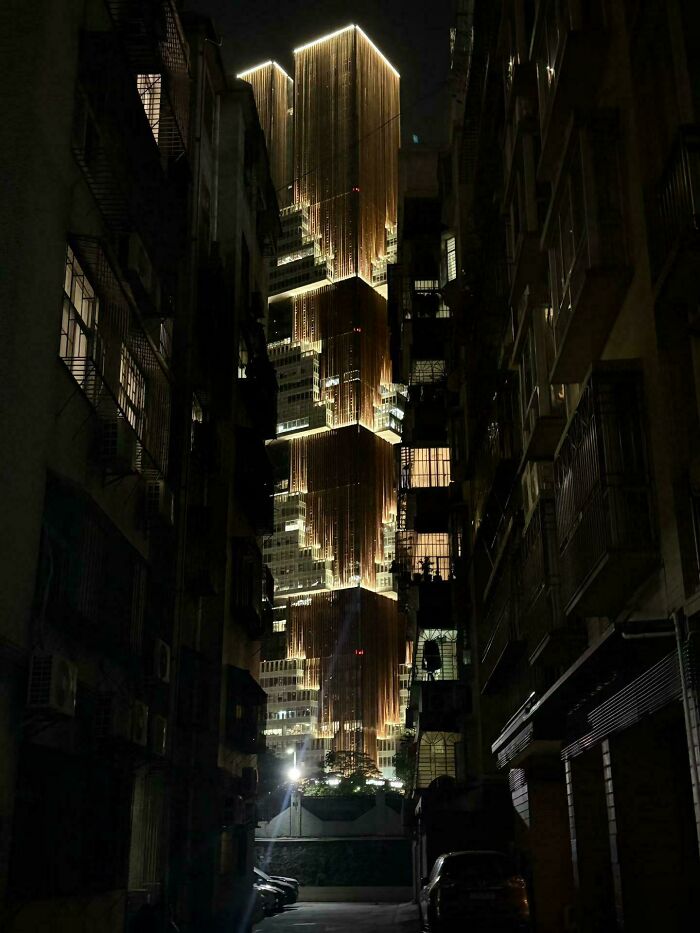 A tall, brightly lit building with gold accents, seen from a dark alley, a perfect evil mastermind's building.