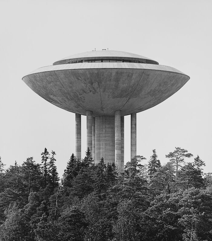 A concrete, UFO-like building on stilts, emerging above a forest, perfect for an evil mastermind's plans.