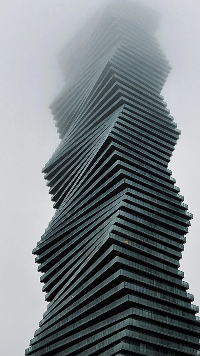 A tall, twisted skyscraper building disappearing into the fog, a fitting lair for an evil mastermind.