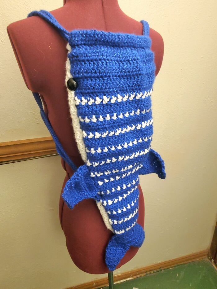 A blue and white crocheted whale shark backpack on a red mannequin, showcasing awesome crocheted detail.