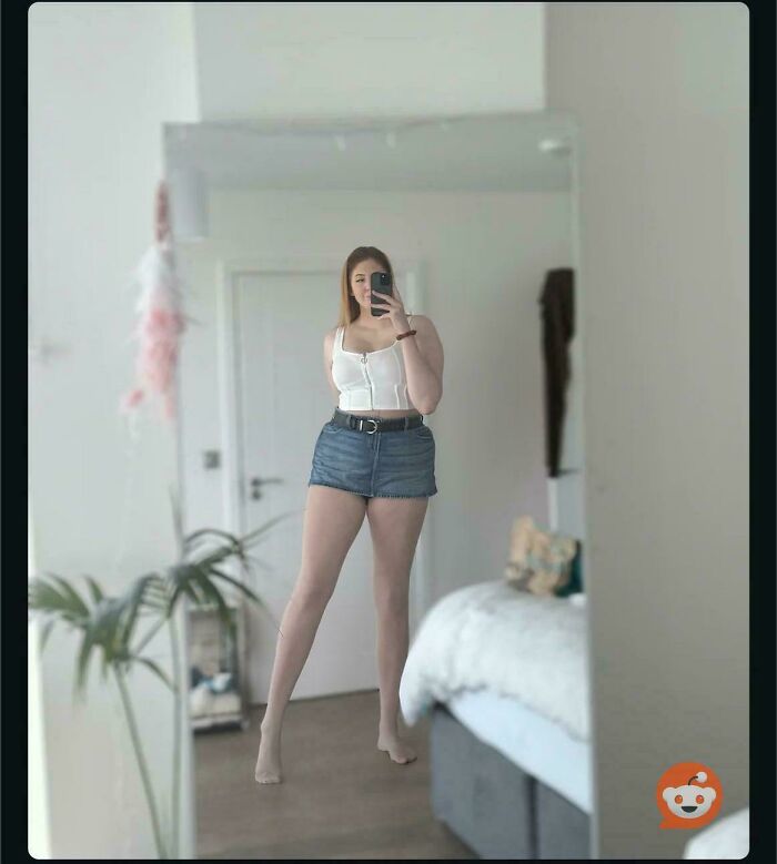 A woman posing in a mirror, her reflection revealing an unnatural pose for social media.