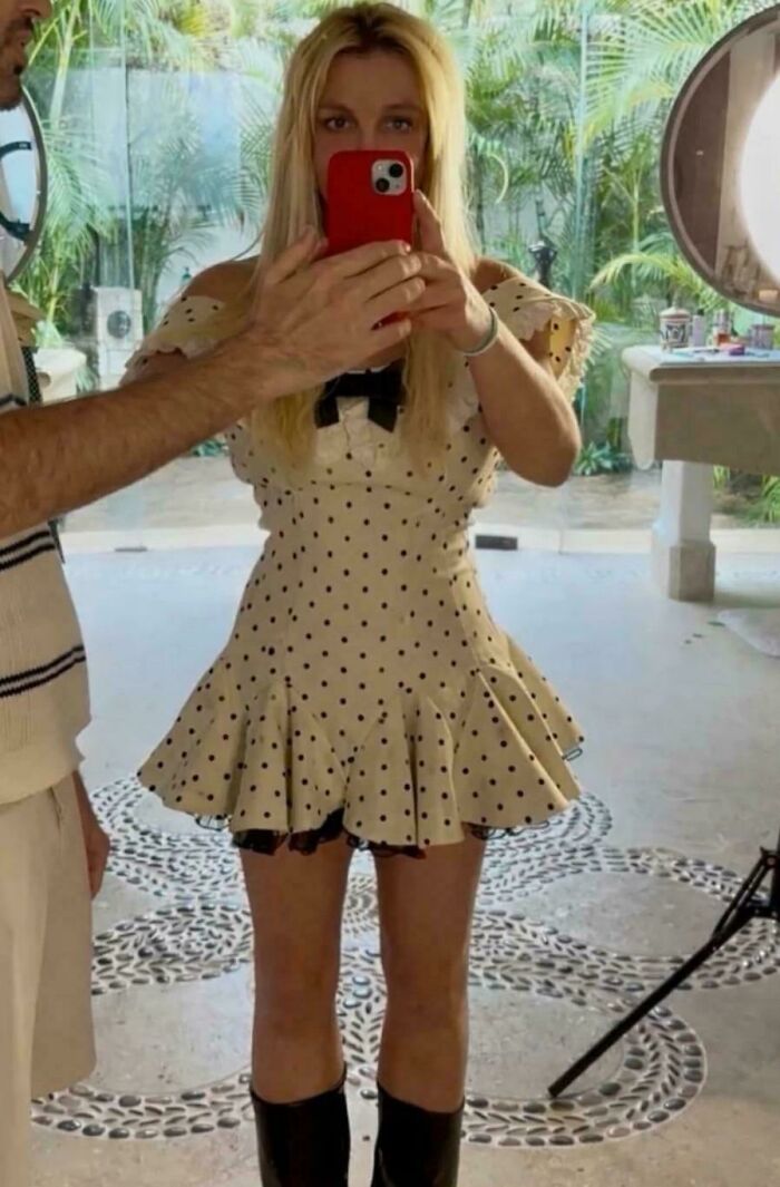 Woman in a polka dot dress taking a mirror selfie, showcasing social media poses.