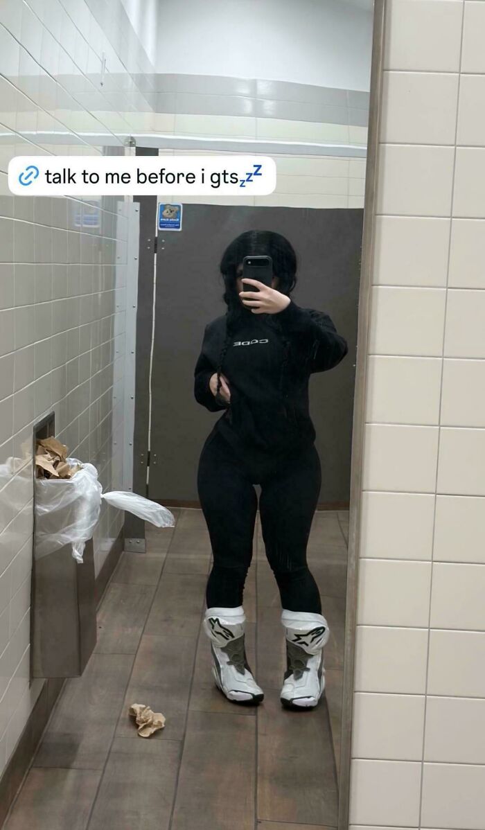 A woman in a black hoodie and pants takes a mirror selfie, attempting to look natural on social media.