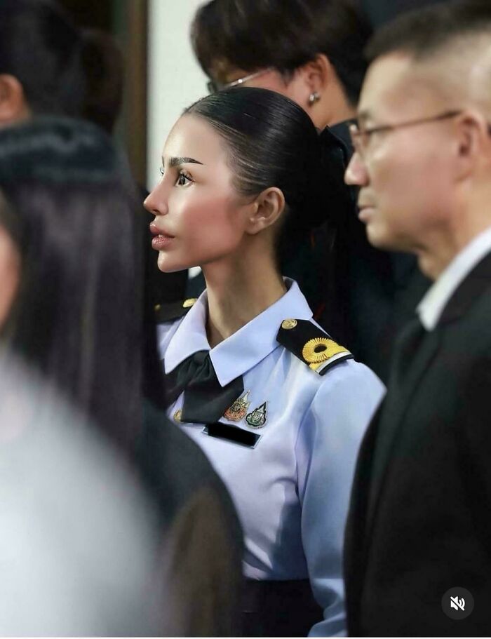 A woman in a uniform stands in profile, looking natural on social media in a crowded setting.