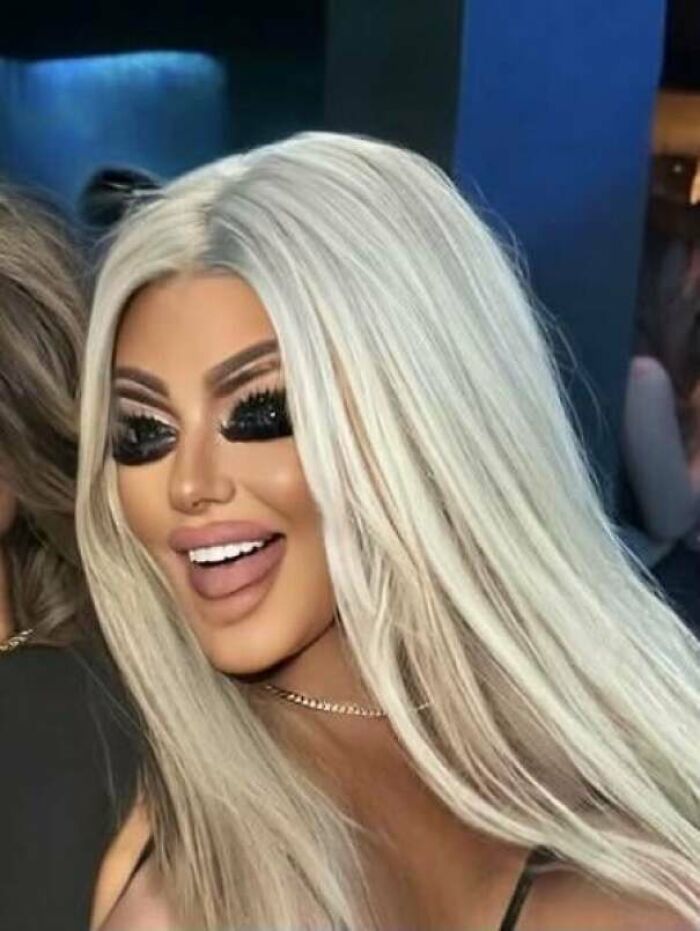 Woman with long blonde hair and heavy makeup, not looking natural on social media, with exaggerated eyes.