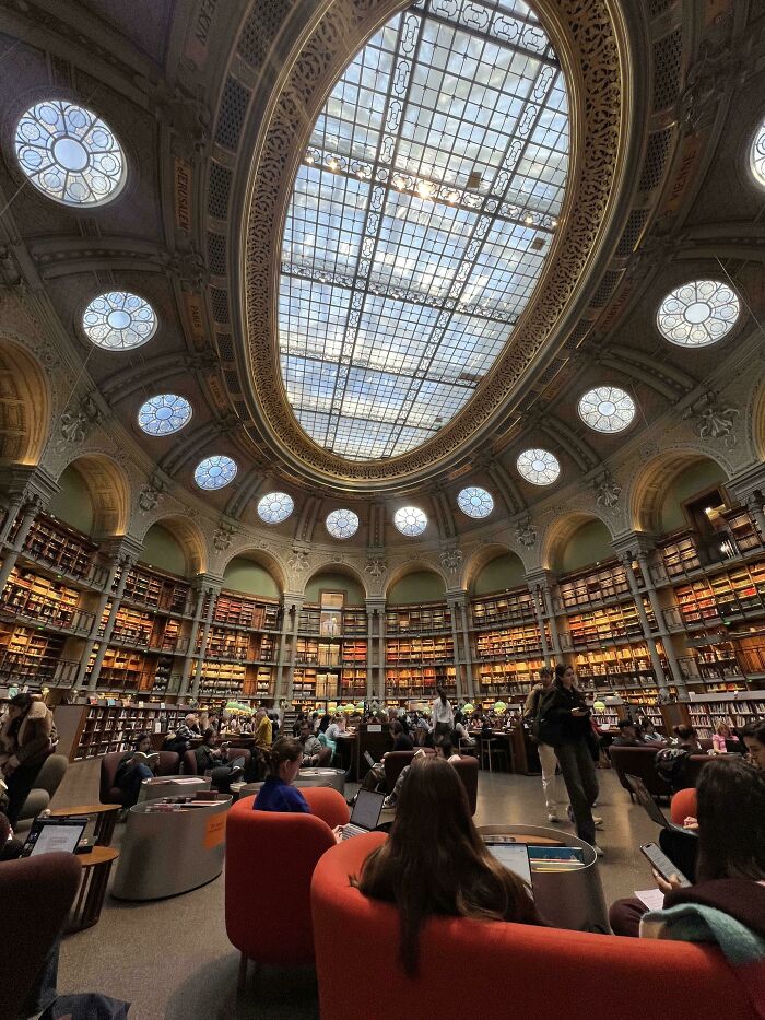 Interior of a beautiful library, showcasing stunning architecture with a grand glass ceiling and numerous bookshelves.