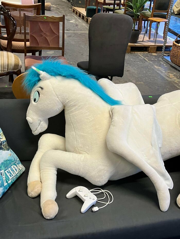 A large white Pegasus plush toy with blue hair, a jackpot find, rests on a couch in a thrift store.