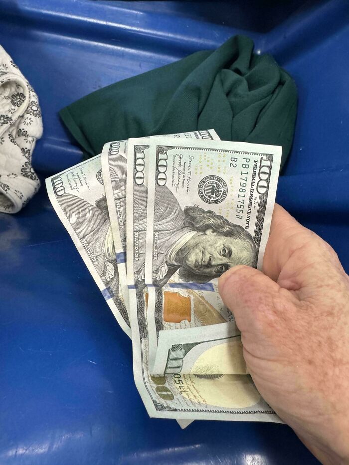 A hand holding several hundred-dollar bills, a surprising thrift store jackpot.