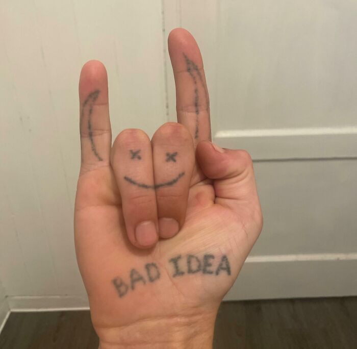 Hand showing bad tattoos on fingers and palm, including a smiley face and the words bad idea.